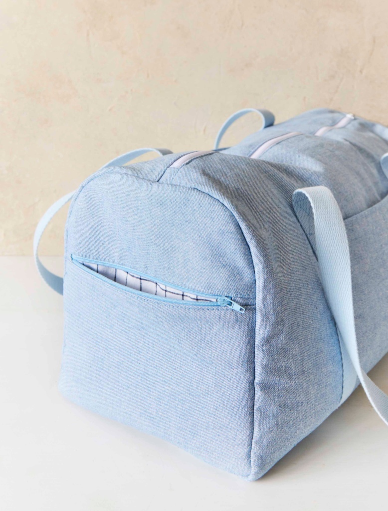Pale blue denim sports bag with pocket zip open to show blue and white checked lining