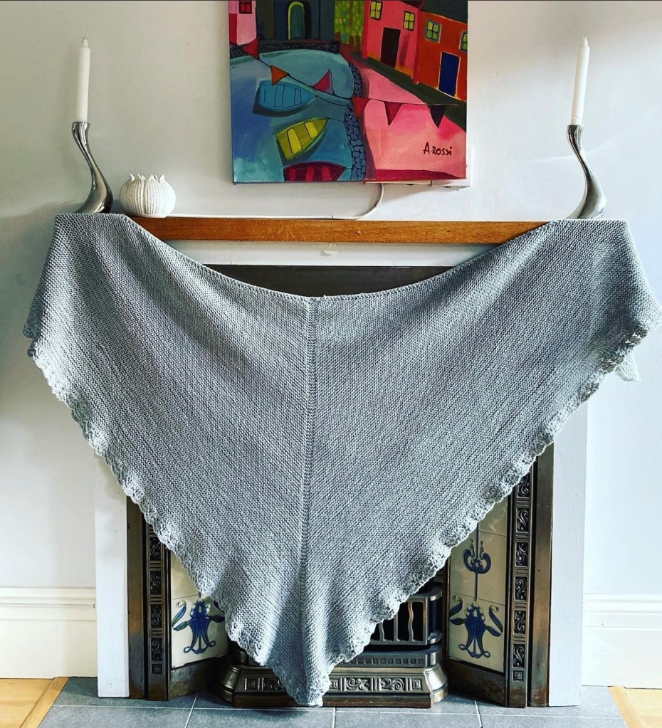 Photo of a triangular knitted shawl displayed on the mantelpiece of an open fire
